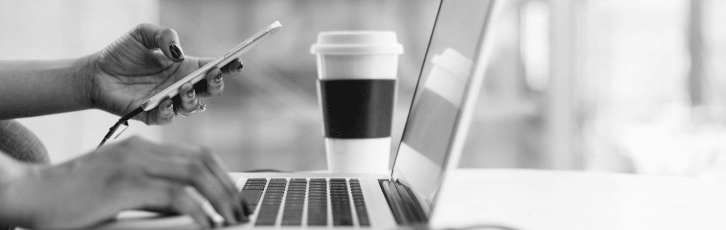 person holding a cellphone in front of an open laptop next to a to-go coffee cup
