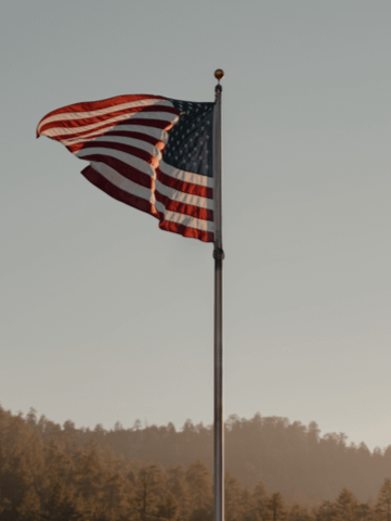 a US flag blowing in the wind on a tall pole