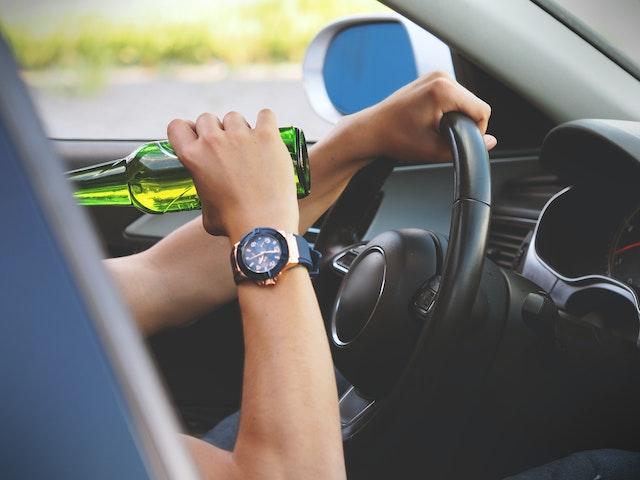 person drinking from glass bottle while driving a car