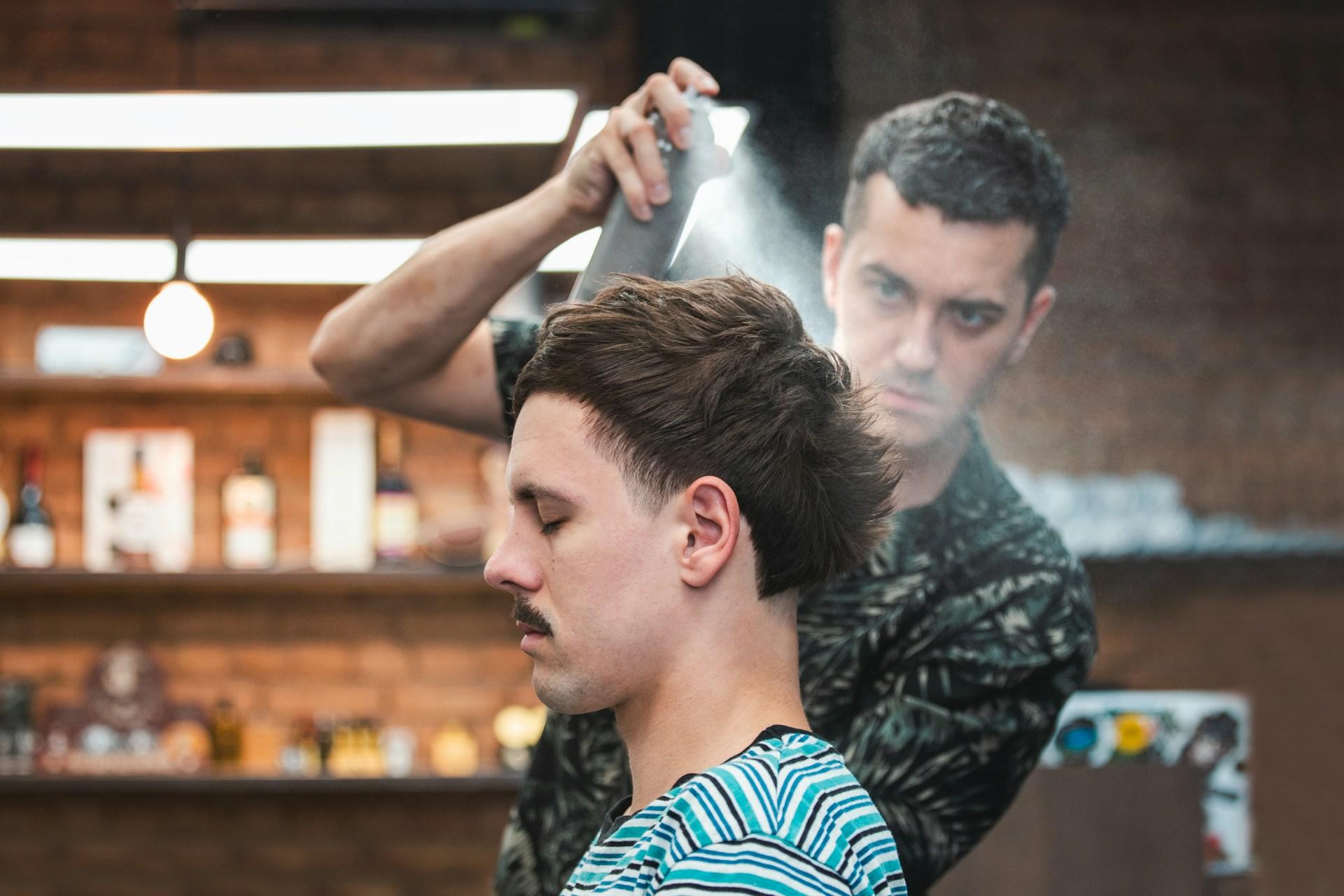 barber spraying man's hair with hairspray