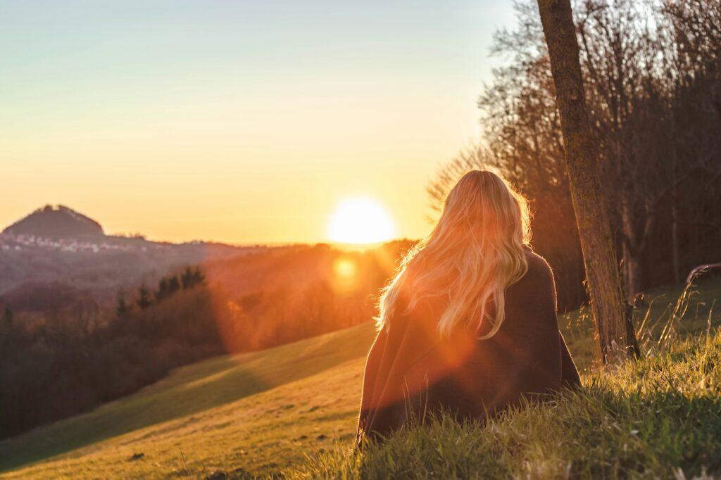 a woman sitting on a hillside watching the sun rise