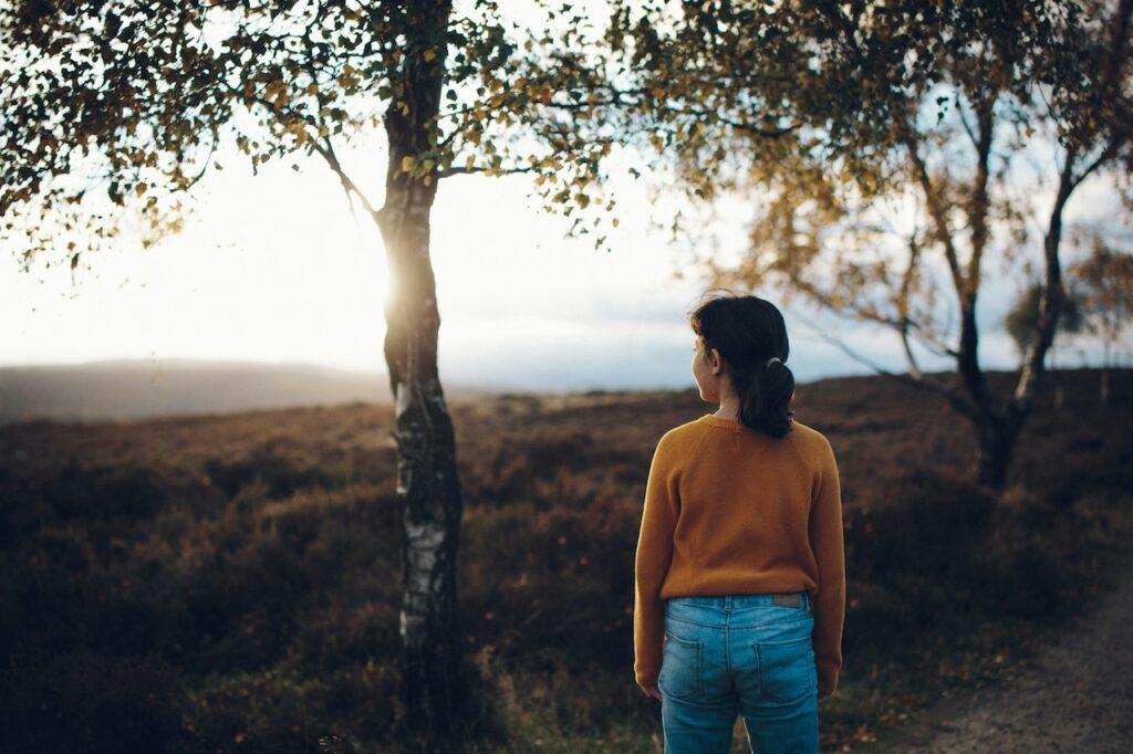 a woman with her back to the viewer looks out over a grassy plain